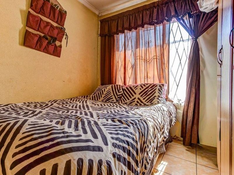 A compact bedroom featuring tiled flooring, a built-in wardrobe, and a window fitted with a security gate.