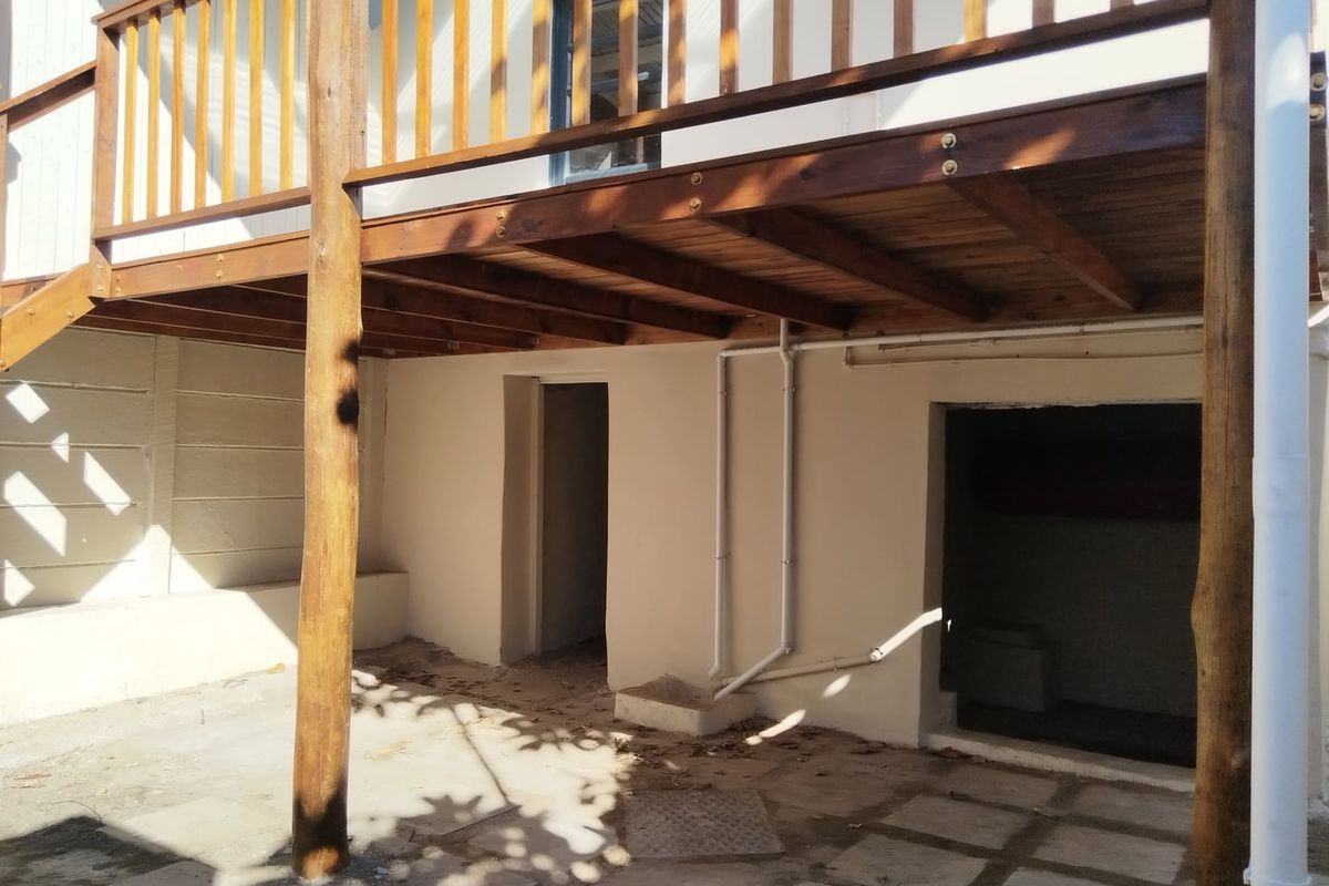 Rear exterior view featuring a raised wooden deck with balustrade over a paved patio area with access to lower level utility spaces.