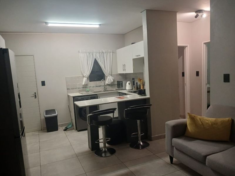 Open-plan kitchen and living area featuring modern cabinetry, a breakfast bar, and tiled flooring, creating a functional and connected living space.