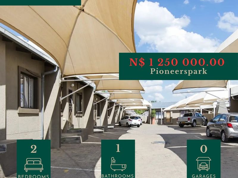 Exterior view of a townhouse complex featuring paved driveway access and installed shade sail carports for resident parking.