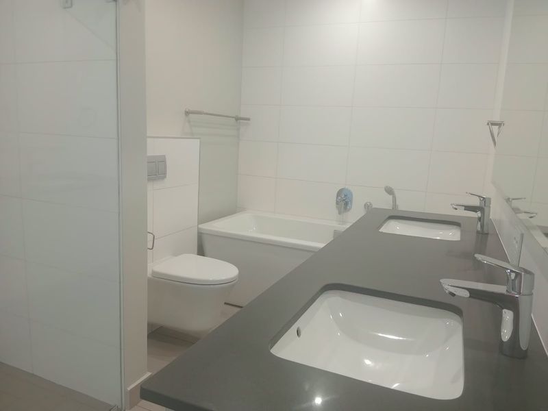Modern bathroom featuring a double vanity with dark stone countertop, wall-hung toilet with concealed cistern, and a built-in bathtub with white wall tiling.