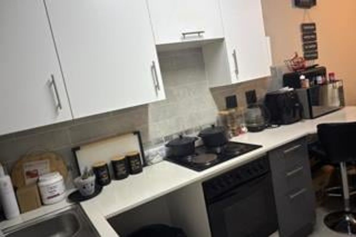 A functional kitchen featuring white upper cabinetry, dark lower drawers, a built-in oven with electric hob, and a tiled backsplash.
