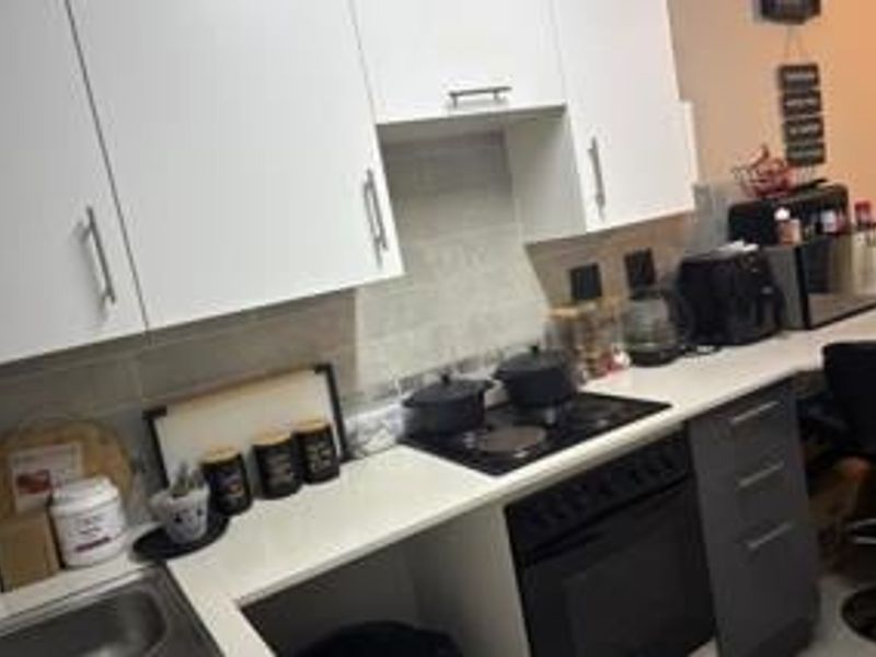 A functional kitchen featuring white upper cabinetry, dark lower drawers, a built-in oven with electric hob, and a tiled backsplash.