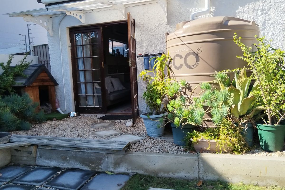 Rear exterior view featuring a water storage tank, filtration system, french doors, and a concrete retaining wall with paved walkway.