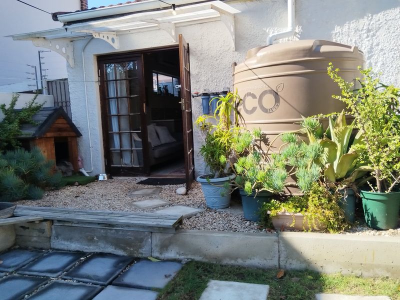 Rear exterior view featuring a water storage tank, filtration system, french doors, and a concrete retaining wall with paved walkway.