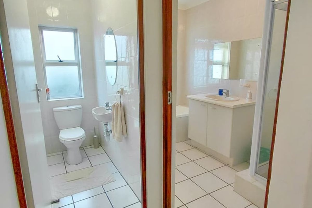 A functional bathroom layout featuring a separate toilet area and a main bathroom with a vanity, shower, and bathtub, finished with white wall tiles.