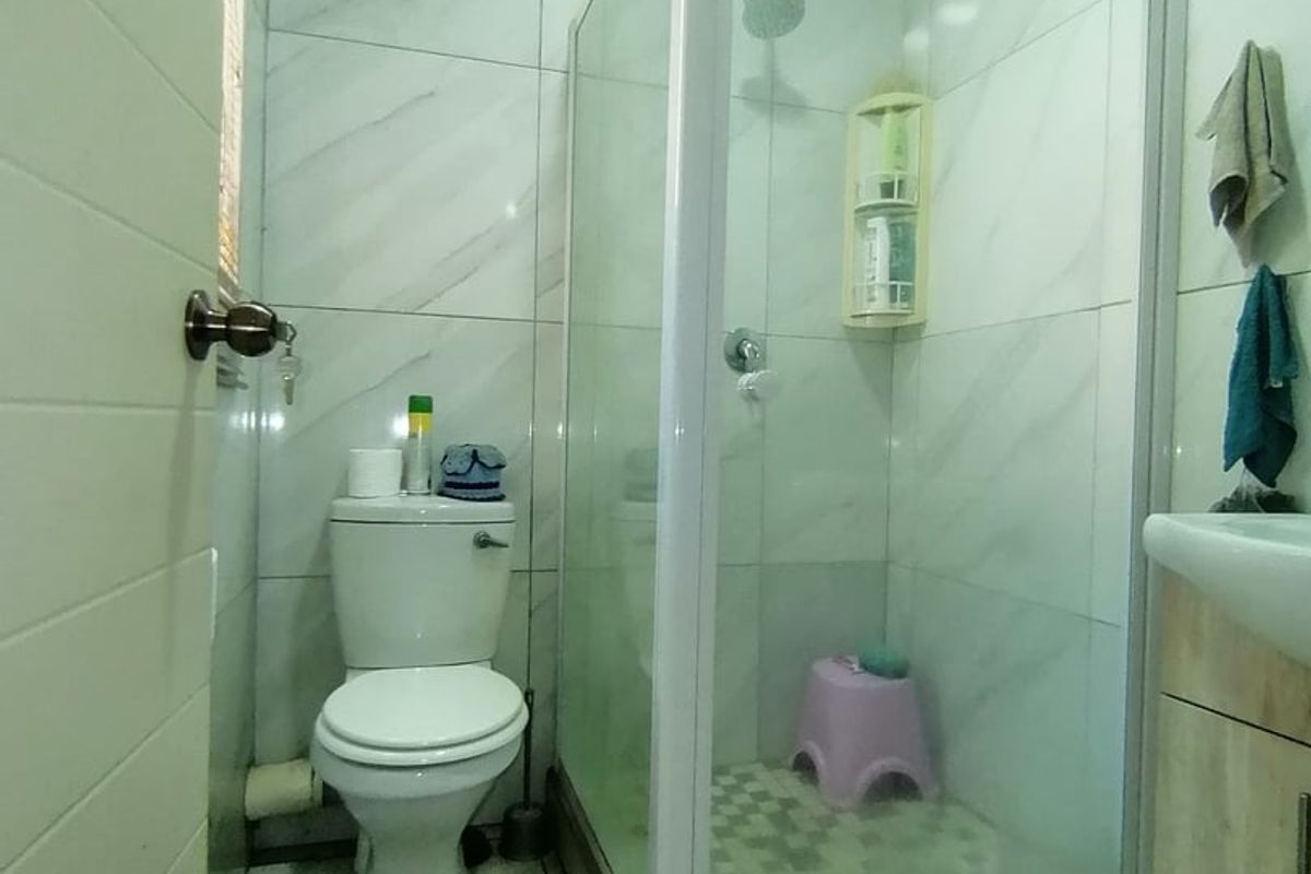 Compact bathroom featuring a glass-enclosed shower, white toilet, and a vanity unit with a washbasin, finished with modern marble-look wall tiles.