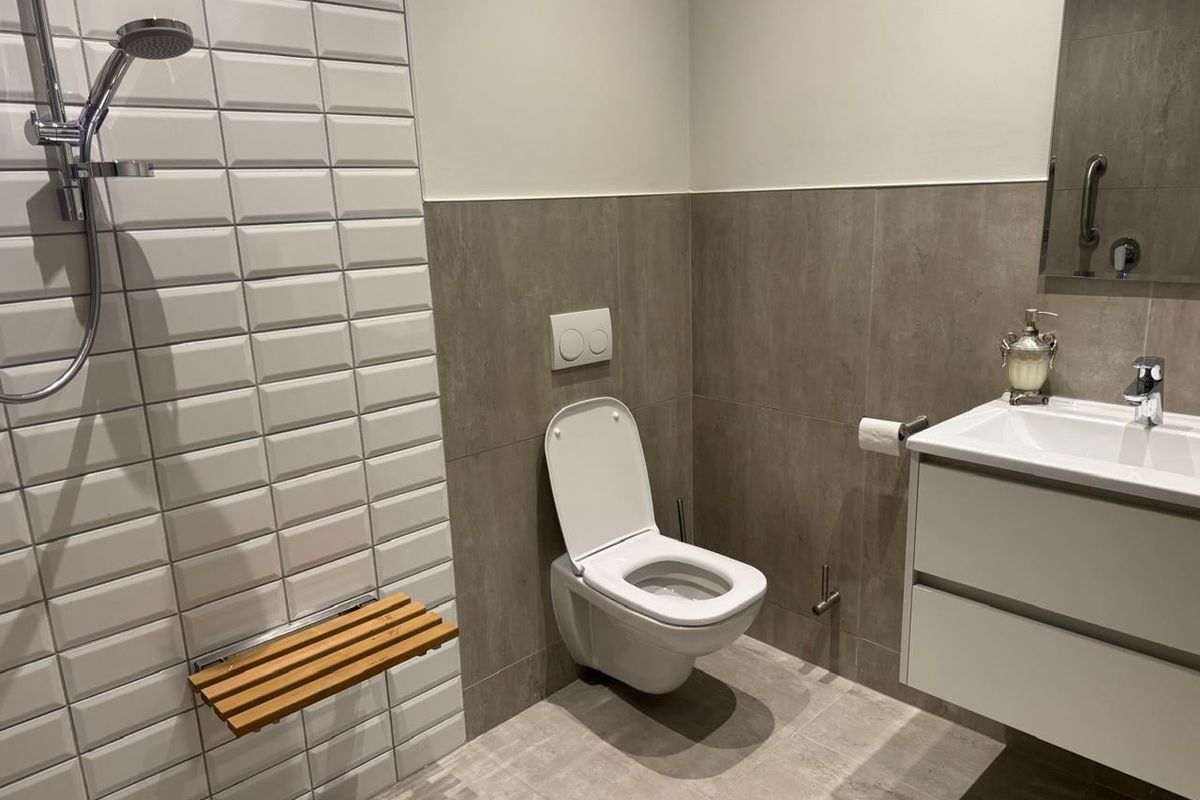Modern bathroom featuring a wall-mounted toilet, vanity unit, and a walk-in shower area with a built-in wooden shower seat and contemporary tiling.