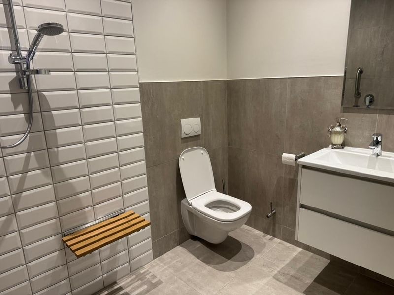 Modern bathroom featuring a wall-mounted toilet, vanity unit, and a walk-in shower area with a built-in wooden shower seat and contemporary tiling.