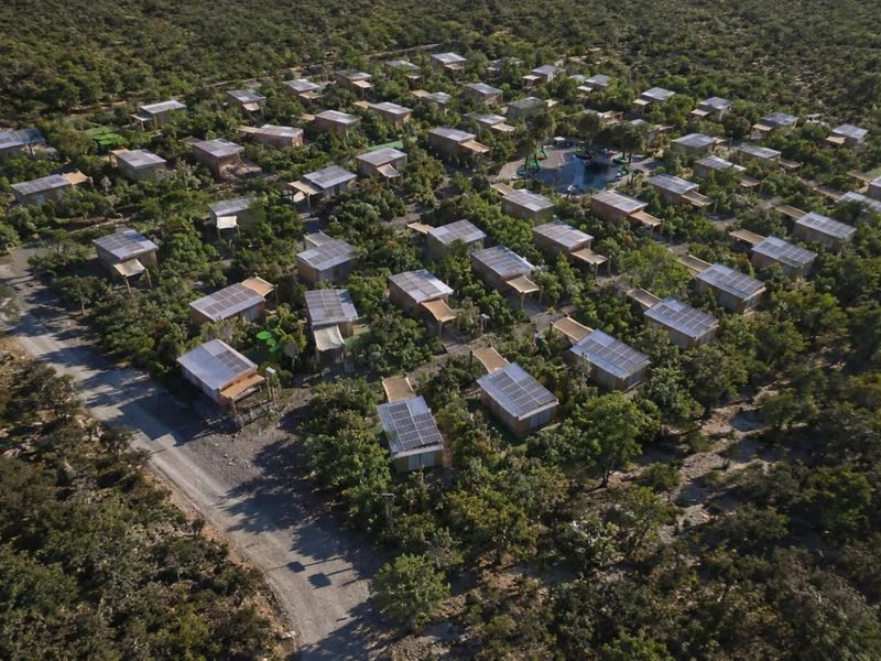 Aerial view of a lodge resort complex featuring multiple individual units with solar panel installations, surrounded by natural vegetation and a central pool area.