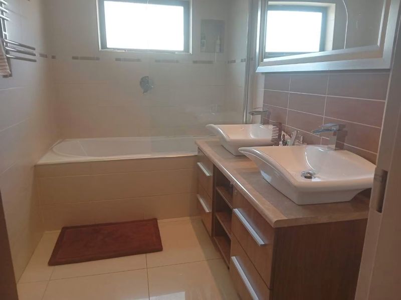 A well-maintained bathroom featuring a double vanity with vessel sinks, a built-in bathtub with a glass screen, and neutral wall and floor tiling.