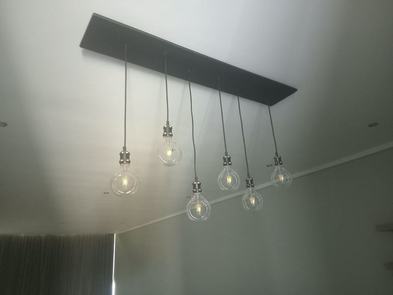 A close-up view of a modern multi-pendant light fixture mounted on a ceiling, featuring exposed filament bulbs.