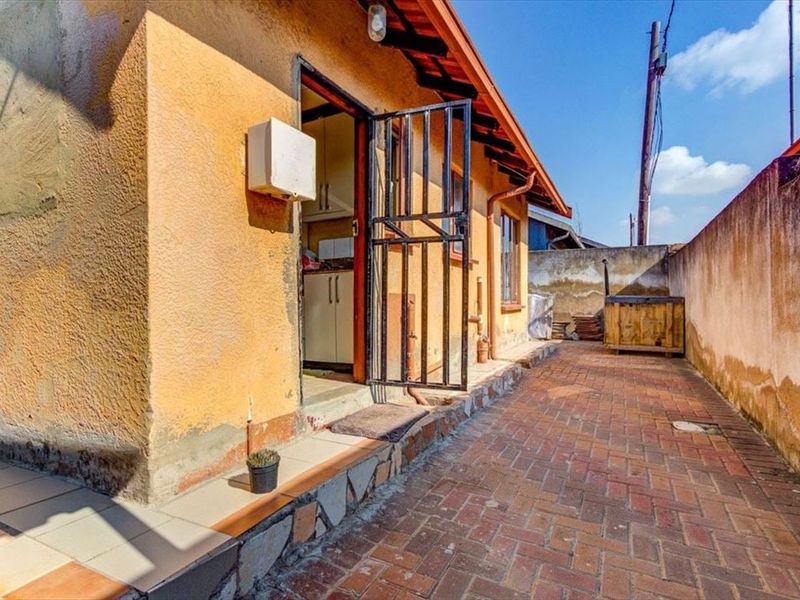 Rear exterior view showing a paved courtyard area with a security gate entrance and weathered wall finishes.