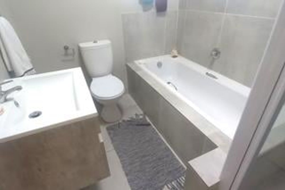 A functional bathroom featuring a built-in vanity, a standard toilet, and a bathtub with wall tiling.