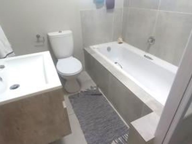 A functional bathroom featuring a built-in vanity, a standard toilet, and a bathtub with wall tiling.