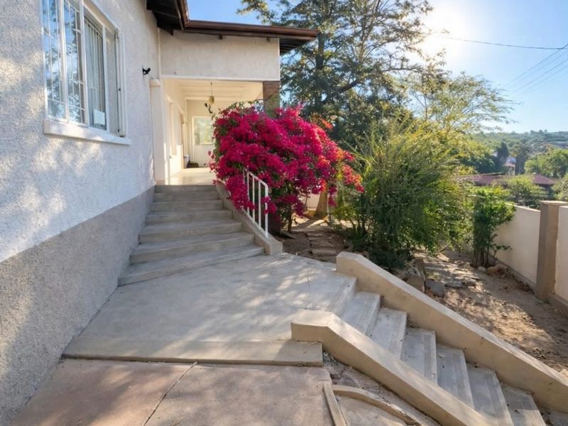 Rear exterior view featuring a concrete staircase leading to a covered patio area with established garden surroundings.