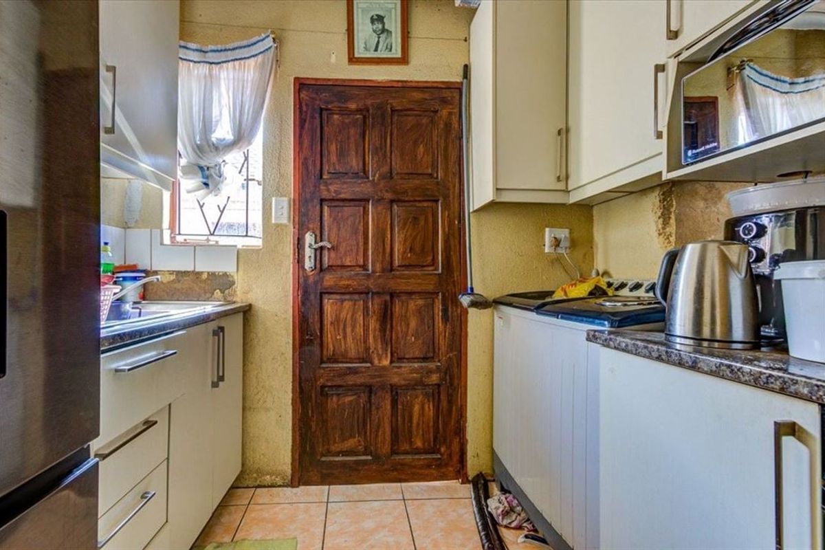 A compact kitchen featuring built-in cabinetry, laminate countertops, and a stainless steel sink, requiring cosmetic updates to the wall finishes and general maintenance.