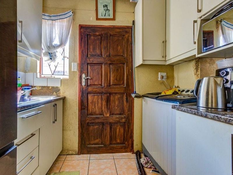 A compact kitchen featuring built-in cabinetry, laminate countertops, and a stainless steel sink, requiring cosmetic updates to the wall finishes and general maintenance.
