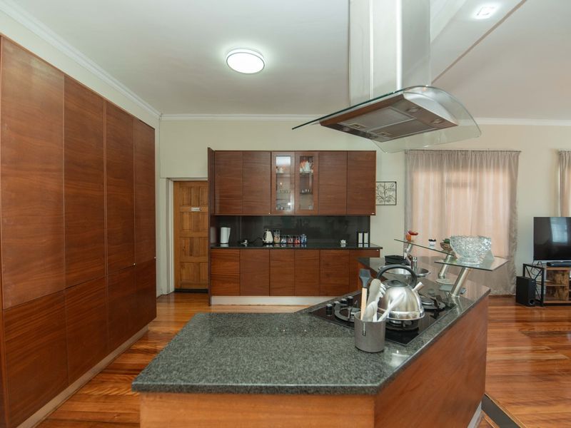 Open-plan kitchen featuring dark wood cabinetry, granite countertops, a central island with a gas hob, and polished hardwood flooring throughout the living space.