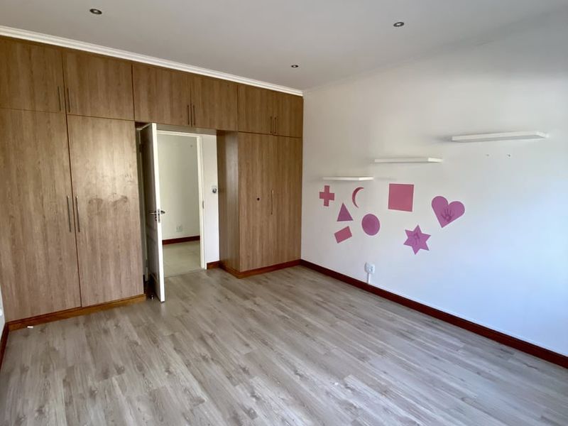 A bright, empty bedroom featuring wood-look laminate flooring, extensive built-in cabinetry, and recessed ceiling lighting.