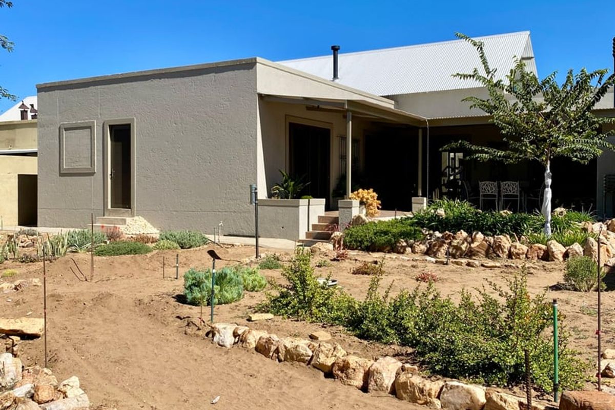 Rear view of the property featuring a covered patio, stucco exterior, and a landscaped garden area with rock borders.