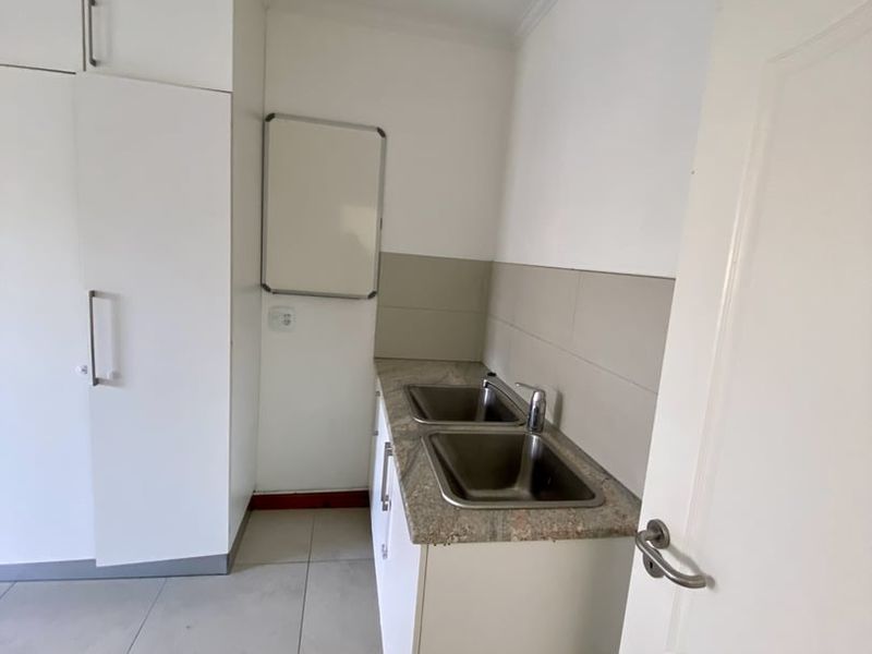 A clean and functional scullery area featuring built-in cabinetry, a double stainless steel sink, stone countertops, and neutral tiled flooring.