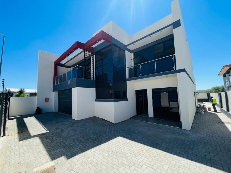 Modern double-storey residential property featuring a paved driveway, glass balustrades, and contemporary architectural design with clean lines and a neutral color palette.