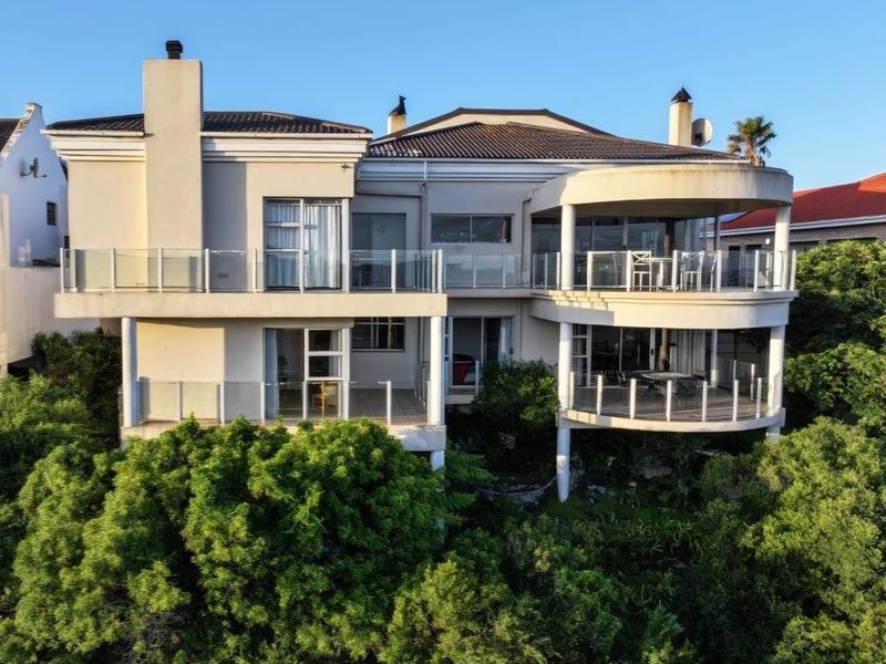 Rear elevation of a multi-story residence featuring expansive balconies with glass balustrades, sliding door access, and established surrounding greenery.