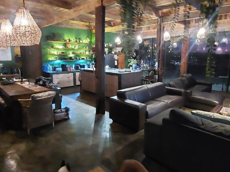 Spacious open-plan living and kitchen area featuring exposed timber beams, polished concrete floors, and large glass doors leading to an outdoor view.