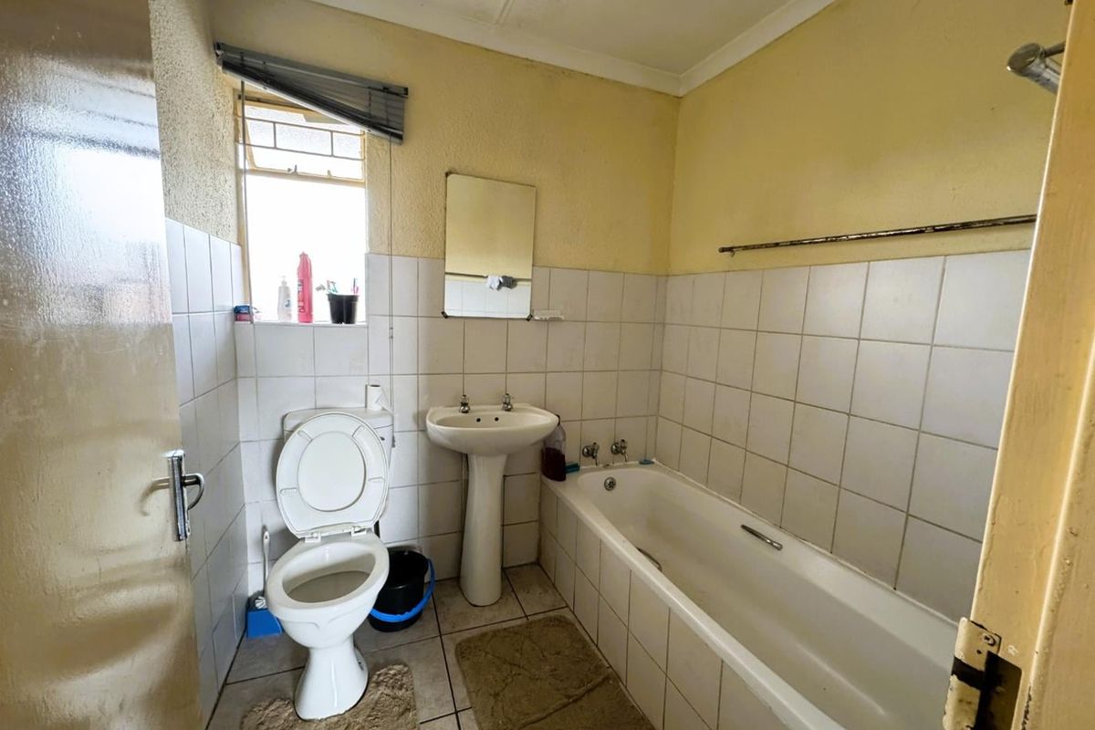 A dated bathroom featuring a standard bathtub, pedestal basin, and toilet with tiled walls and neutral flooring.