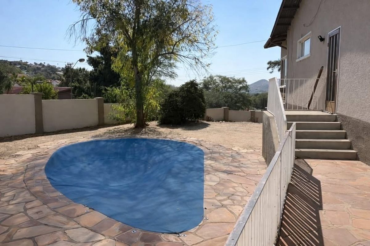 Outdoor pool area featuring a covered swimming pool, stone paved surround, and concrete stairs leading to the main house structure.