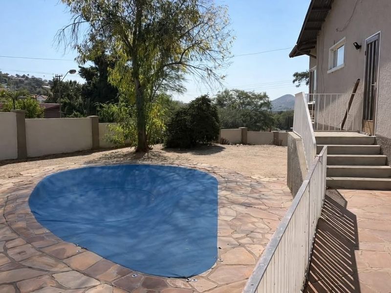 Outdoor pool area featuring a covered swimming pool, stone paved surround, and concrete stairs leading to the main house structure.