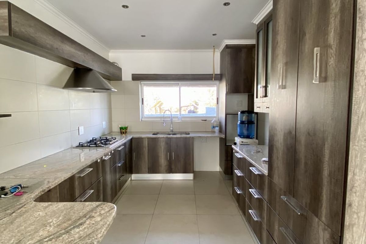 Modern kitchen featuring extensive dark wood cabinetry, granite countertops, a gas hob with extractor fan, and neutral tiled flooring.