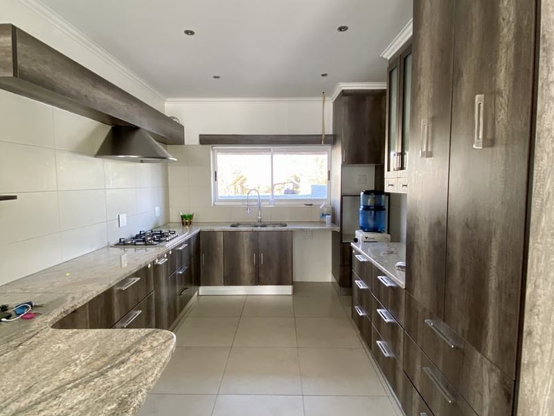 Modern kitchen featuring extensive dark wood cabinetry, granite countertops, a gas hob with extractor fan, and neutral tiled flooring.