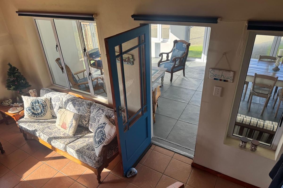 A living area featuring tiled floors and direct access to an outdoor patio through a blue timber door and sliding glass doors.