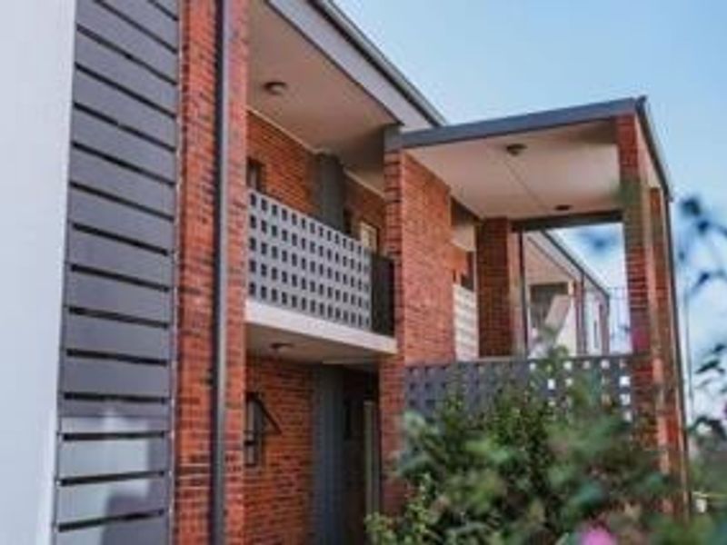 Exterior view of an apartment building featuring a brick facade, private balconies with metal privacy screens, and integrated downlighting.