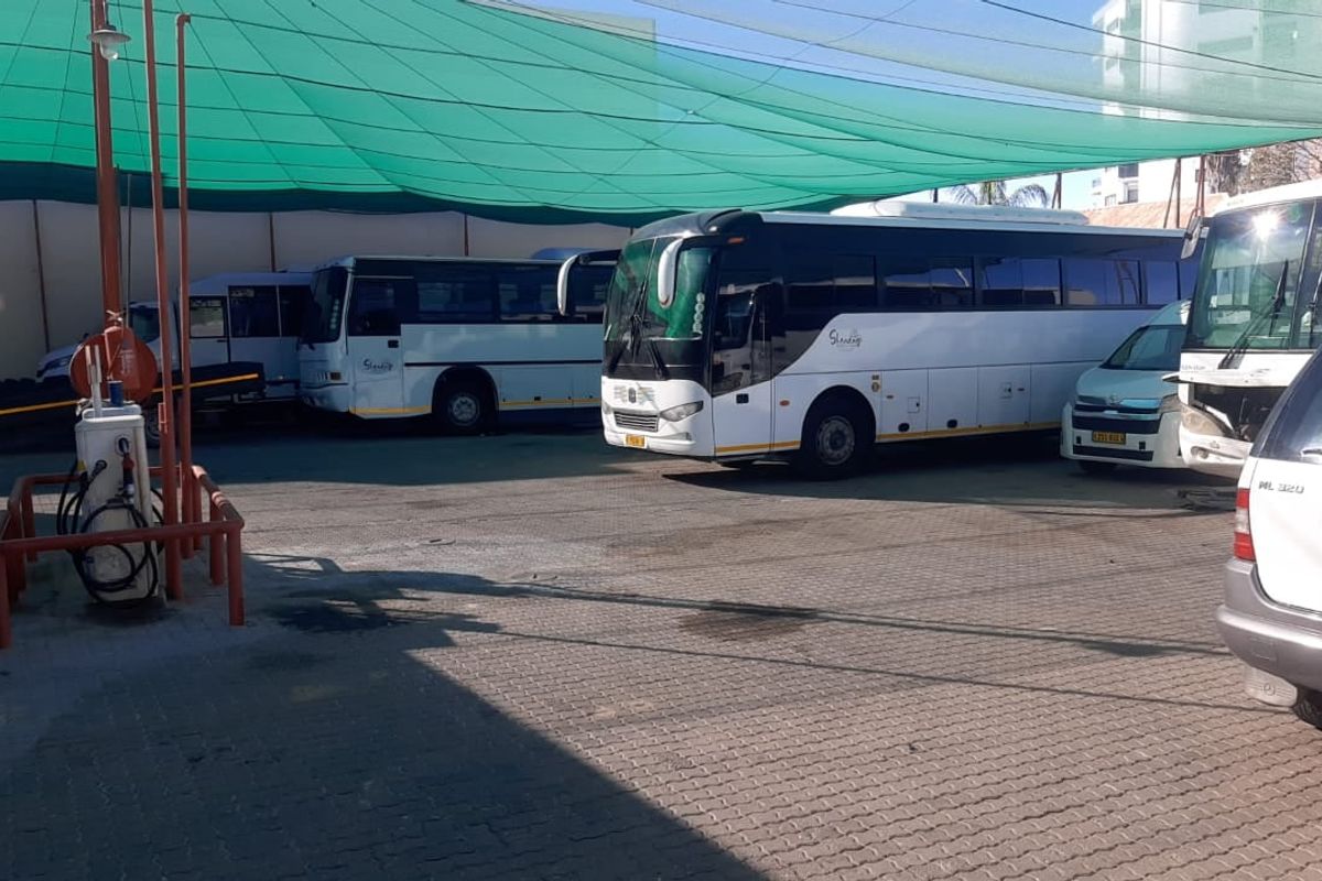 A paved outdoor parking and depot area featuring a shade cloth canopy and a fuel pump station for commercial vehicles.
