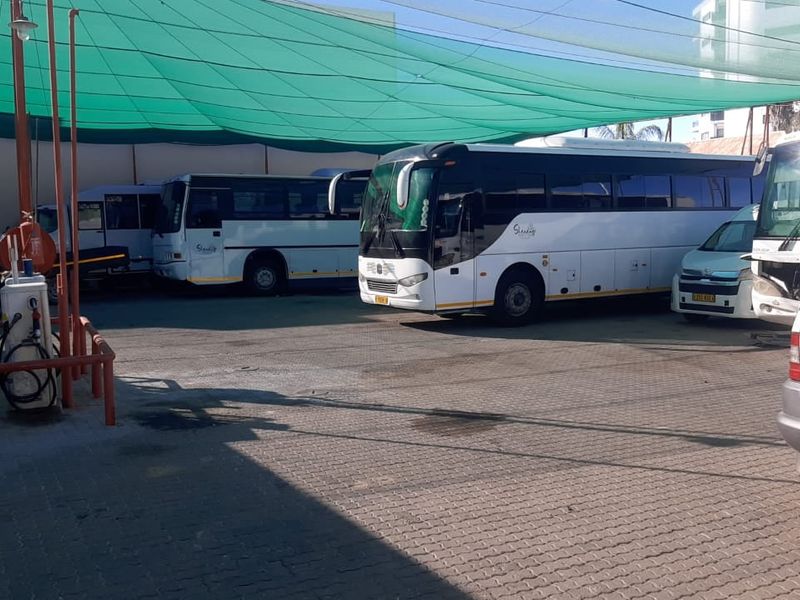 A paved outdoor parking and depot area featuring a shade cloth canopy and a fuel pump station for commercial vehicles.