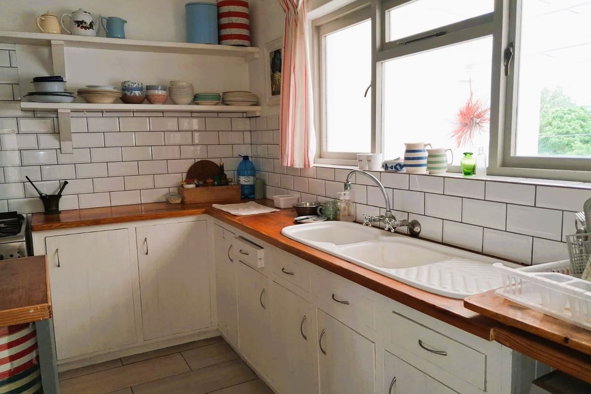 A functional kitchen featuring white cabinetry, timber countertops, subway tile backsplash, and a double basin sink with a view through the window.