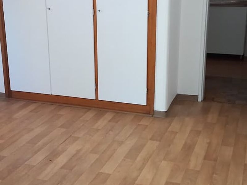 A vacant bedroom featuring built-in cupboards and laminate flooring, with an adjacent doorway leading to a bathroom area.