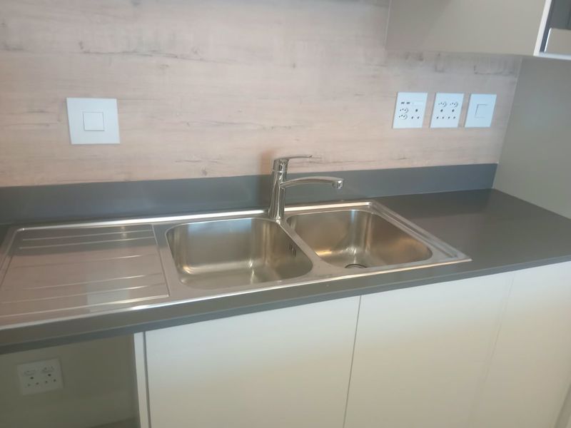 Modern kitchen area featuring a stainless steel double sink, stone countertop, and light wood-look splashback with integrated electrical outlets.