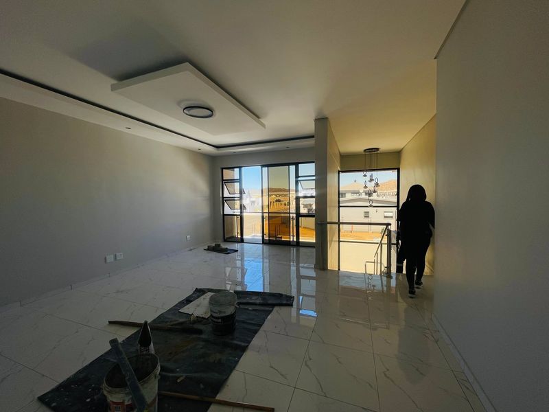 Spacious, modern living area featuring large windows, polished porcelain tiles, and a contemporary recessed ceiling design, currently in the final stages of completion.