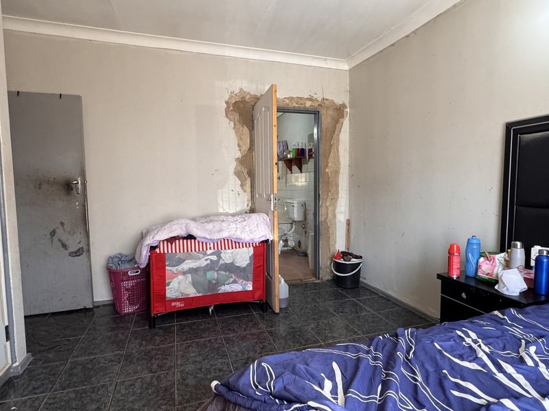Bedroom featuring tiled flooring and coving, currently showing significant wall plaster damage around the doorway and general wear to finishes.