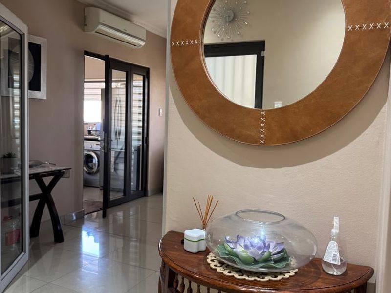 A well-maintained hallway featuring tiled flooring and a wall-mounted air conditioning unit, providing access to an adjacent laundry or utility space.
