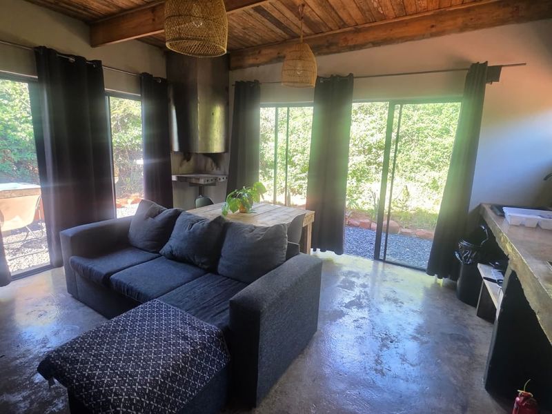 Open-plan living area featuring exposed timber beam ceilings, polished concrete floors, a built-in fireplace, and direct access to the garden through sliding glass doors.