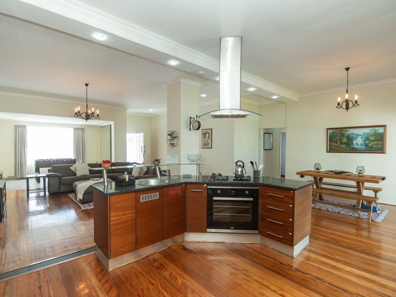 Spacious open-plan living area featuring a central kitchen island with built-in oven, gas hob, and extractor fan, complemented by warm hardwood flooring throughout.