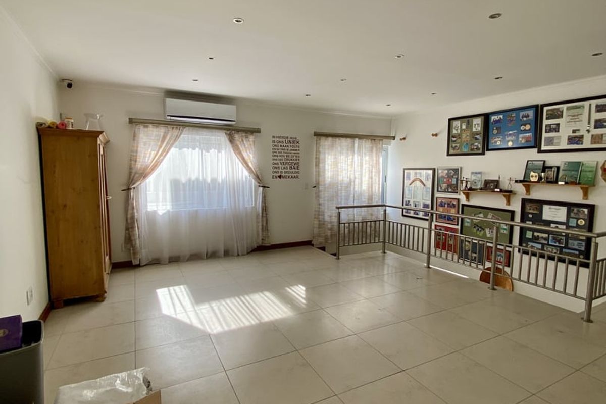 Spacious living area featuring neutral tiled flooring, recessed downlighting, a wall-mounted air conditioning unit, and a metal balustrade overlooking a lower level.