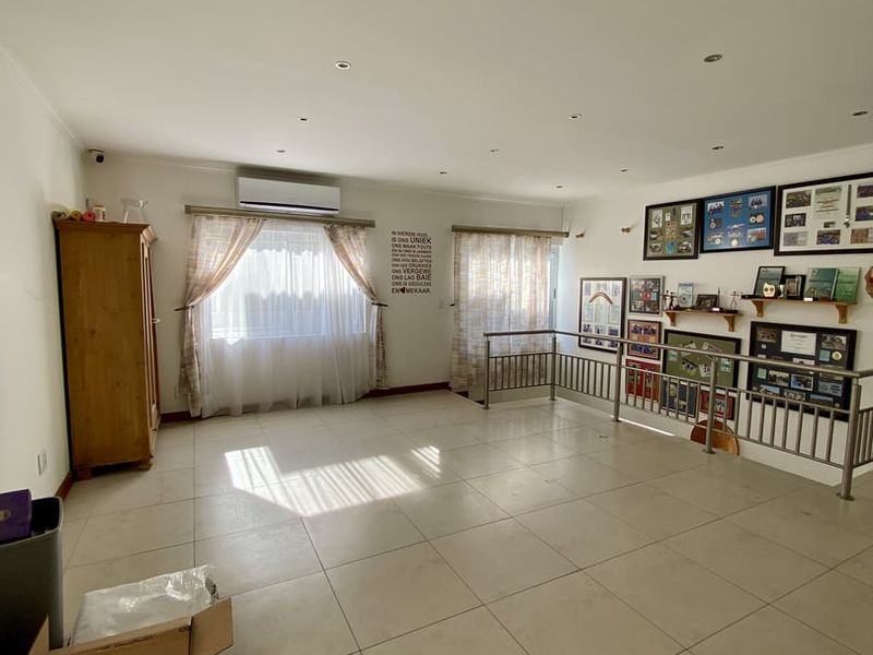 Spacious living area featuring neutral tiled flooring, recessed downlighting, a wall-mounted air conditioning unit, and a metal balustrade overlooking a lower level.