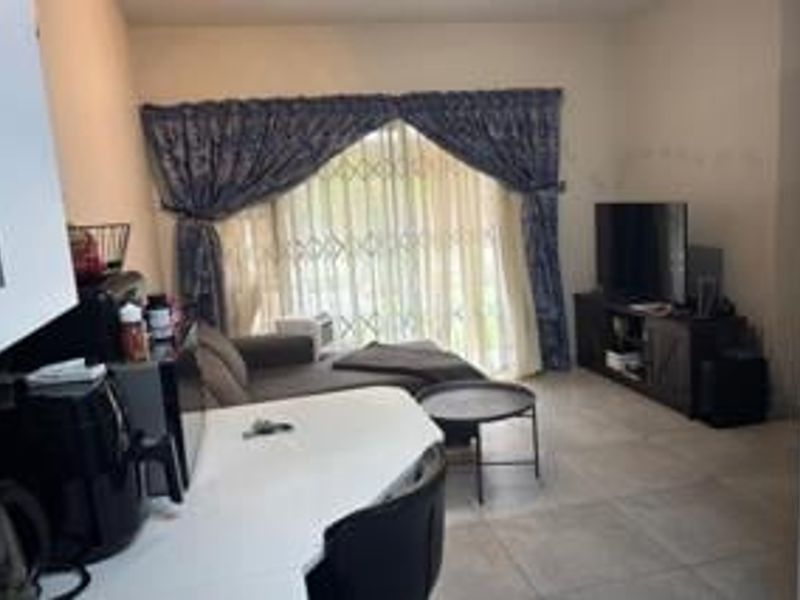An open-plan living area featuring tiled flooring and a sliding door with a security gate, providing access to the exterior.