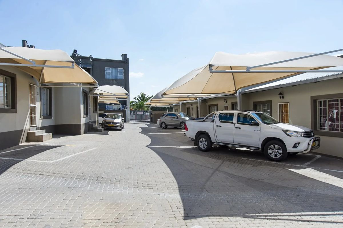 Exterior view of a townhouse complex driveway featuring paved parking areas and installed shade cloth carports for vehicle protection.
